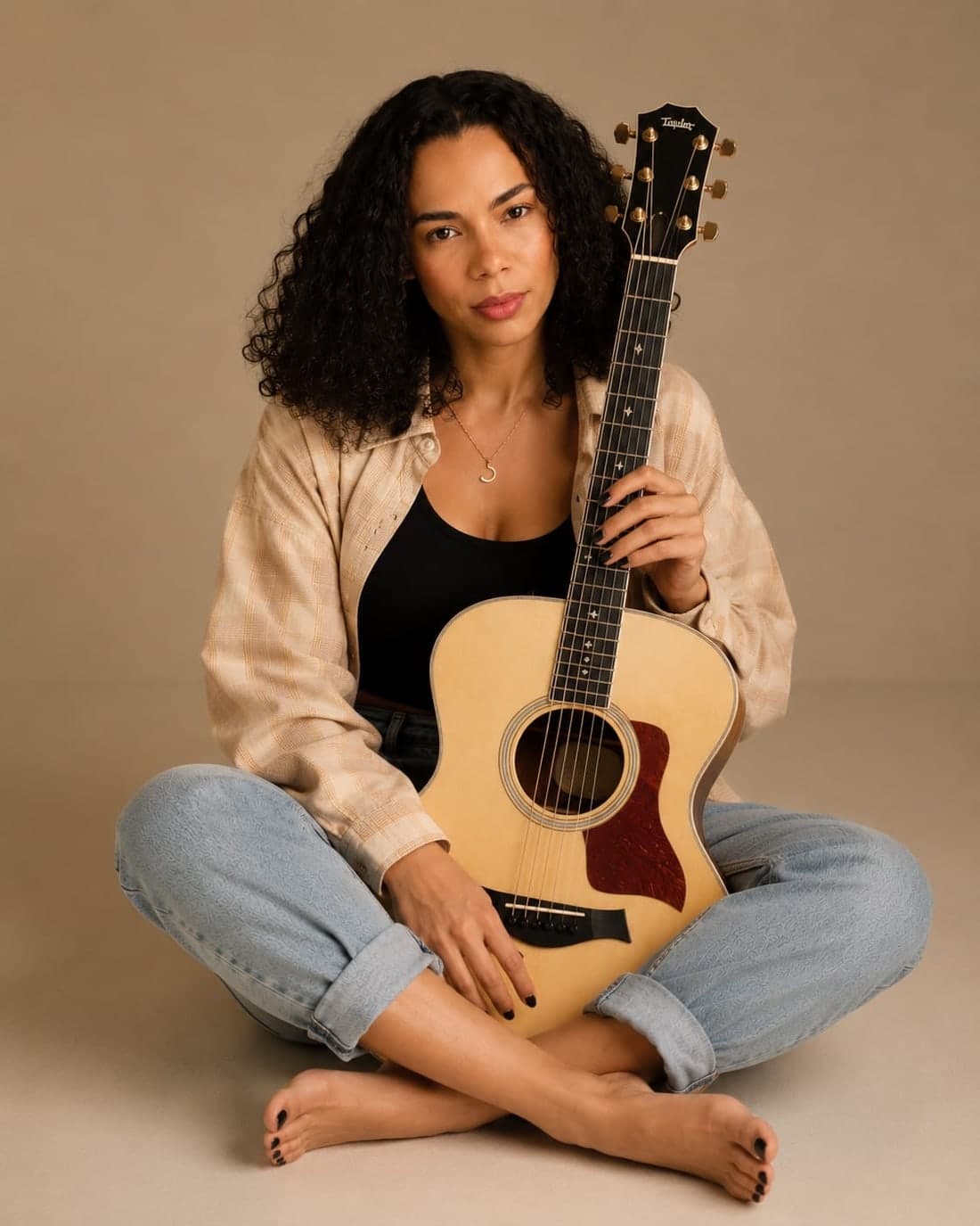 Gabriela Vaz sentada no chão do estúdio, com o violão no colo